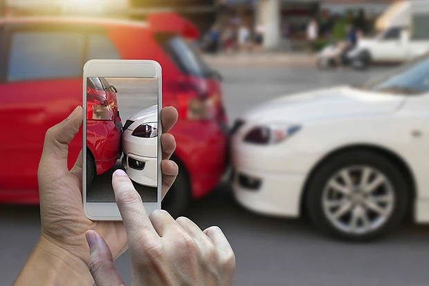 A person photographing two damaged cars with a smartphone.