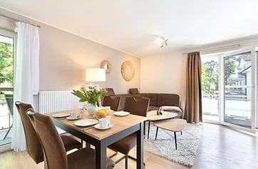 Hell eingerichteter Wohn- und Essbereich der Ferienwohnung Helene mit gedecktem Esstisch und Balkontür