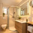 Badezimmer mit Dusche, Waschtisch und beleuchtetem Spiegel