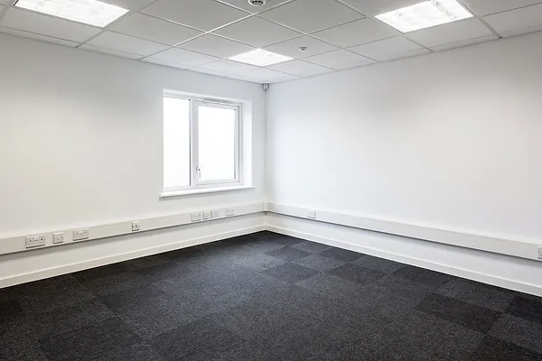 An empty commercial office with grey carpet and a drop-tile ceiling