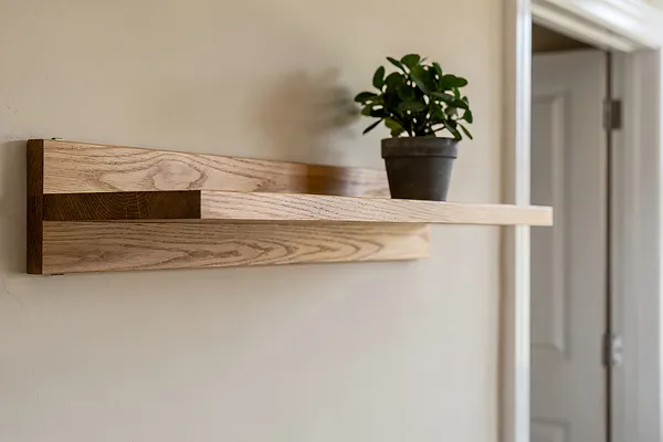 A light-oak floating shelf with a potted plant on a warm neutral wall