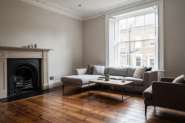 A living room with a fireplace, sash window and wooden floorboards