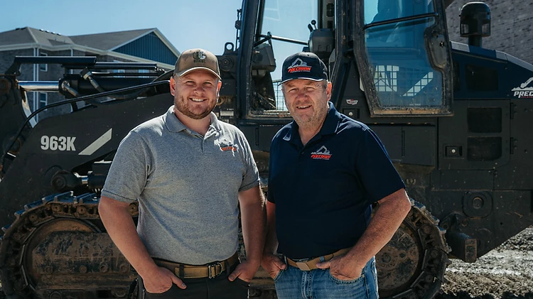 Precision Excavating & Grading leadership standing in front of a Caterpillar 963K track loader on a residential jobsite