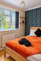 The Oakwood bedroom with wooden bed, orange bedding and teal floral feature wall
