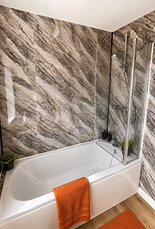 The Elmwood bath and overhead shower with marble-effect walls and orange towels