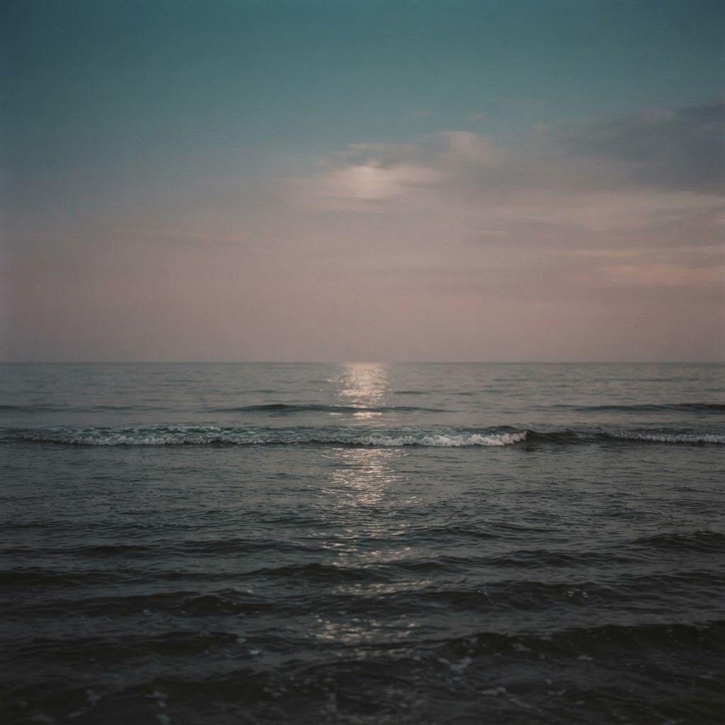 A calm sea at dusk under a soft gradient sky of deep teal and dusty rose, with a faint path of moonlight on the water