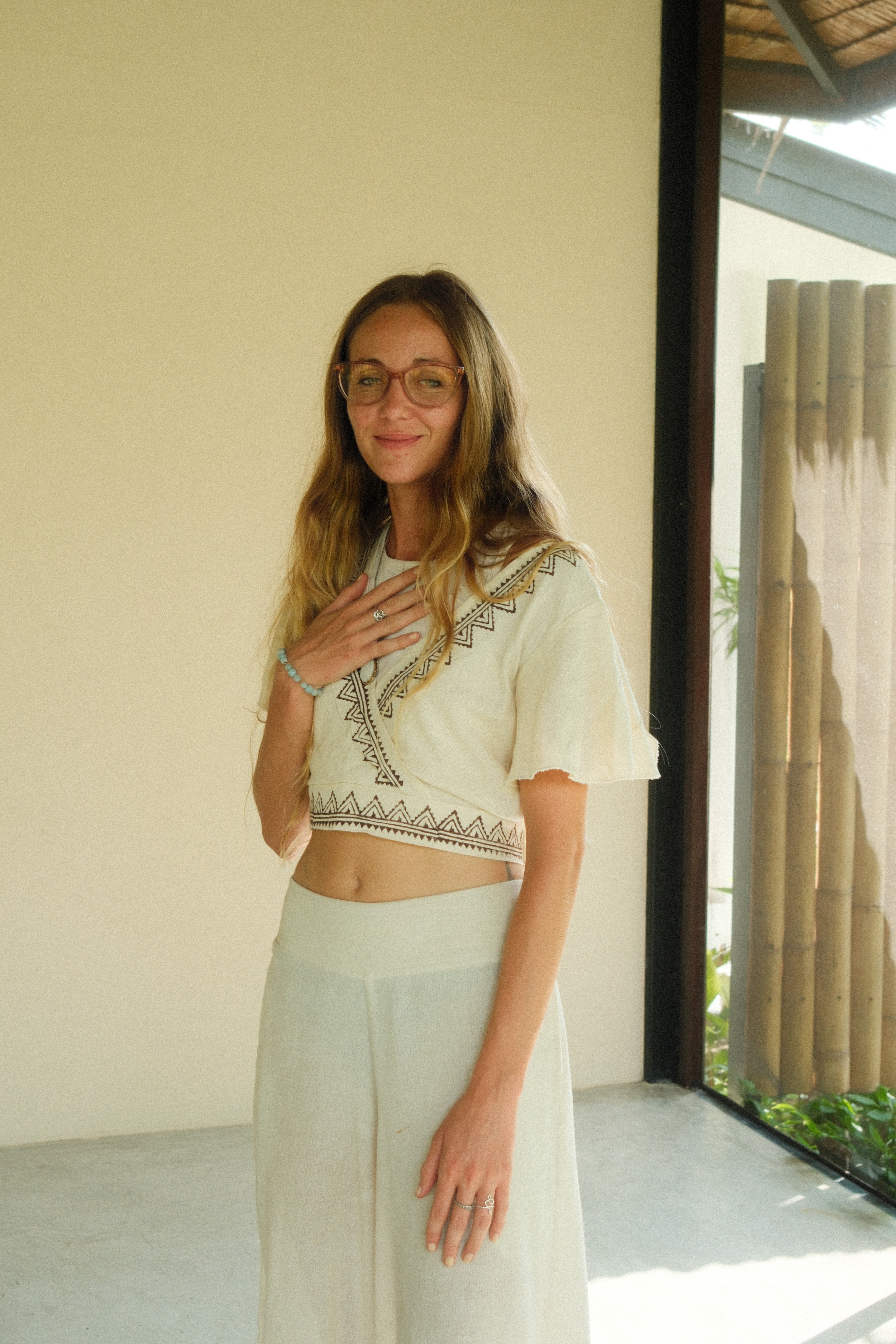 Sofi standing indoors in a cream patterned top, one hand resting over her heart