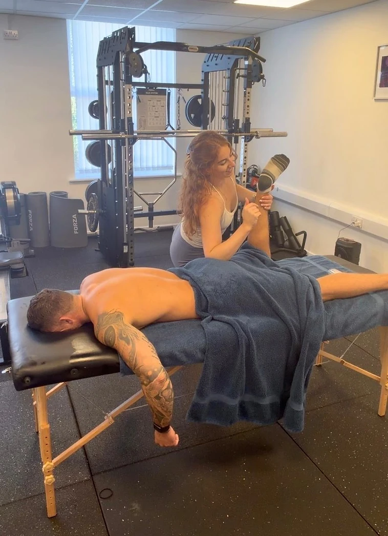 Kate giving a client an assisted hamstring stretch on a massage table at Crew42 gym in Crosby