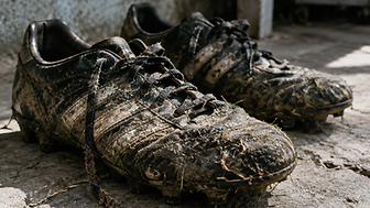 Botas de fútbol embarradas sobre el piso de concreto