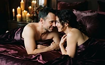 A couple lying close on dark satin sheets in whispered conversation