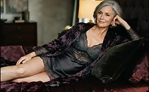 A mature woman in elegant lingerie reclining on dark satin