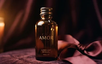 A glass bottle of lubricant beside a silk ribbon on dark velvet