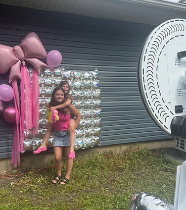 Two girls sharing a piggyback ride beside the ring-light photobooth setup