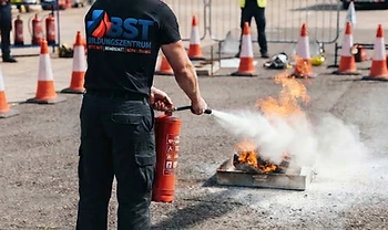 Praktische Löschübung mit rotem Feuerlöscher im Freien, von hinten fotografiert