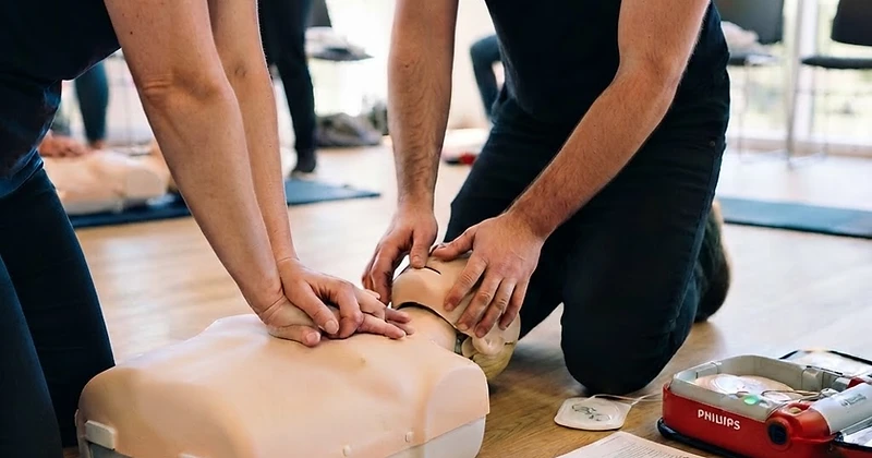 Hände üben die Herzdruckmassage an einer Übungspuppe in einer hellen Schulungsfläche