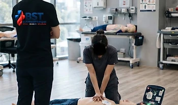 Teilnehmer übt von hinten gesehen die Herzdruckmassage an einer Übungspuppe mit AED-Trainingsgerät