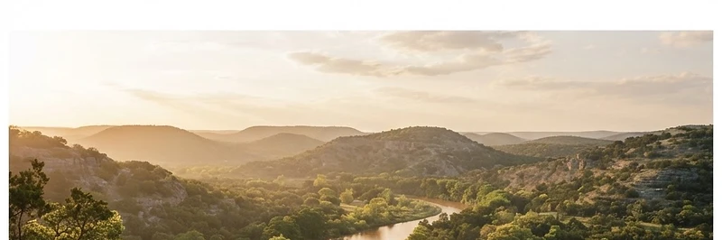 Rolling Texas Hill Country hills with live oaks and a cypress-lined river at golden hour