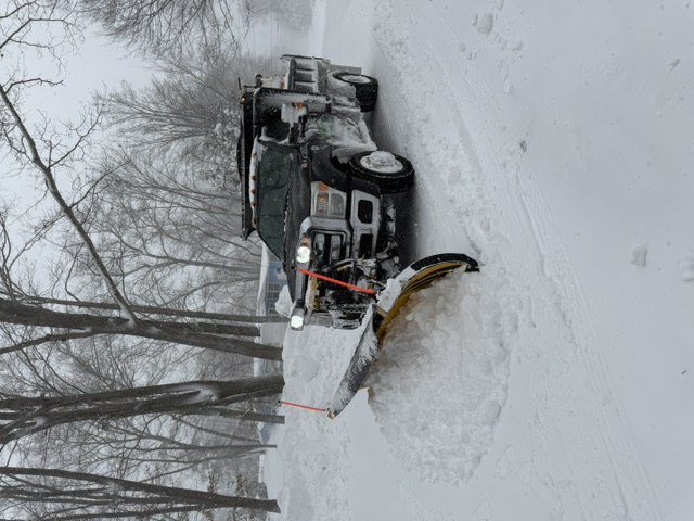 Snow plow truck with sander clearing a commercial property during a winter storm in Rhode Island