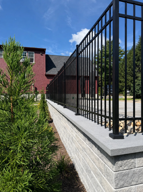 Segmental retaining wall with granite cap and black aluminum fence above a paver patio in North Smithfield, RI