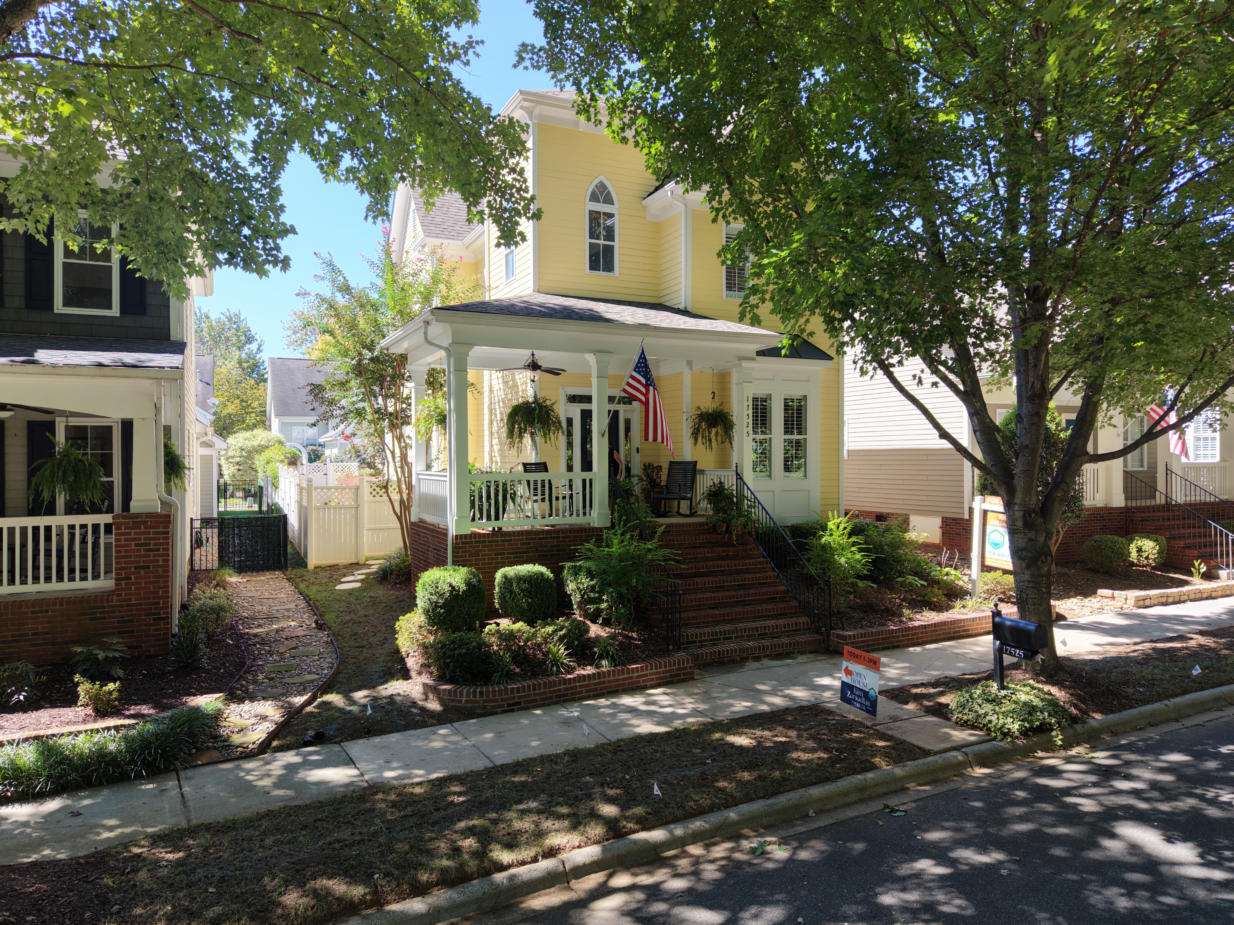 Yellow two-story home with a wraparound front porch and an American flag