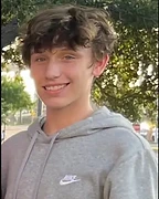 Luke Andrew Rogers smiling outdoors in a gray hoodie.