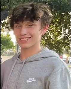 Luke Andrew Rogers smiling outdoors in a gray hoodie.