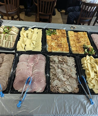 Trays of sandwiches, cold meats, quiche and cheese laid out for a buffet
