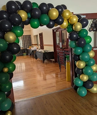 A black, green and gold balloon arch framing the doorway into our events space
