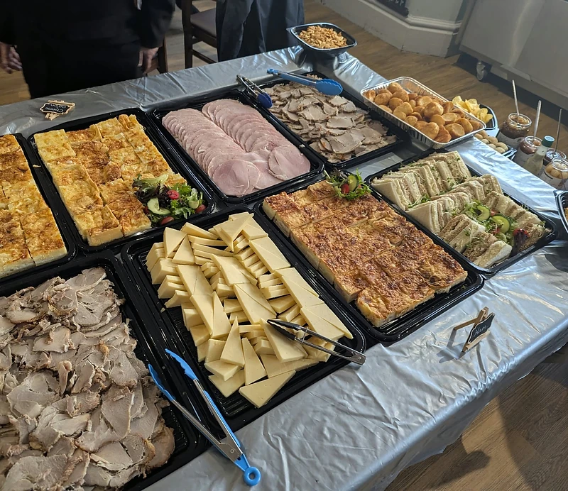 A buffet table laid with sandwiches, cold meats, quiche and cheese for an event
