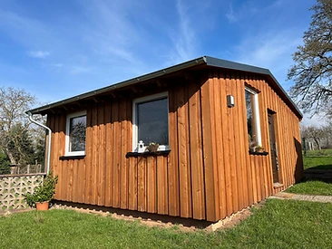 Kleines Gartenhaus mit senkrechter Holzverkleidung und dunklem Satteldach auf dem Rasen