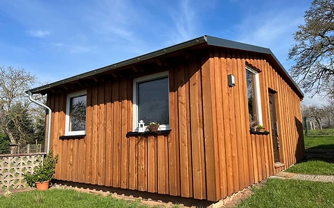 Kleines Gartenhaus mit senkrechter Holzverkleidung und dunklem Satteldach auf dem Rasen