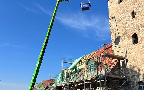 Hubarbeitsbühne hebt Material zu den Dacharbeiten an einem Steinturm