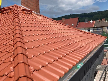 Frisch eingedecktes Terrakotta-Ziegeldach mit First und gemauertem Schornstein