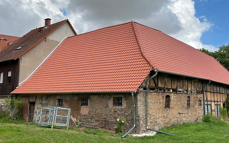 Dasselbe Steingebäude mit neuem rotem Ziegeldach und neuer Entwässerung