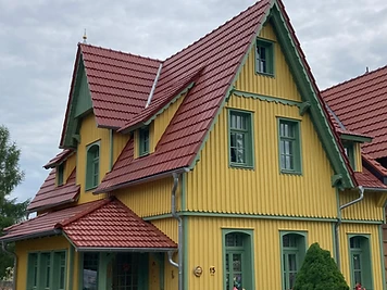 Gelbes Landhaus mit grünen Fensterrahmen, Vorbau und rotem Ziegeldach