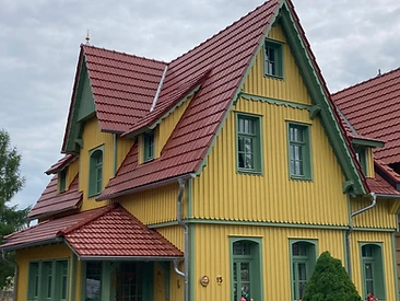 Gelbes Landhaus mit grünen Fensterrahmen, Vorbau und rotem Ziegeldach