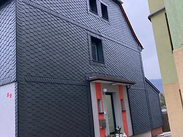 Haus mit dunkler Schiefer-Schindelfassade, orangefarbenen Fensterakzenten und rotem Ziegeldach