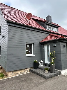 Eingang eines Hauses mit dunkler Holzfassade, rotem Ziegeldach und Zierlaternen