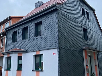 Eckansicht eines Hauses mit Schieferfassade, Putzflächen und Ziegeldach