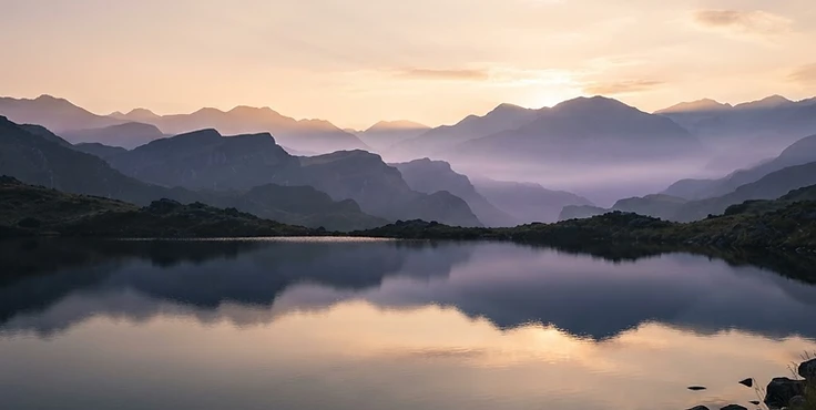 Mystical sunrise over misty violet mountains and a tranquil lake