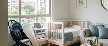A stroller, baby cot and high chair arranged in a bright living room