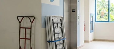 A hand trolley and folding tables stacked neatly beside an HDB lift lobby