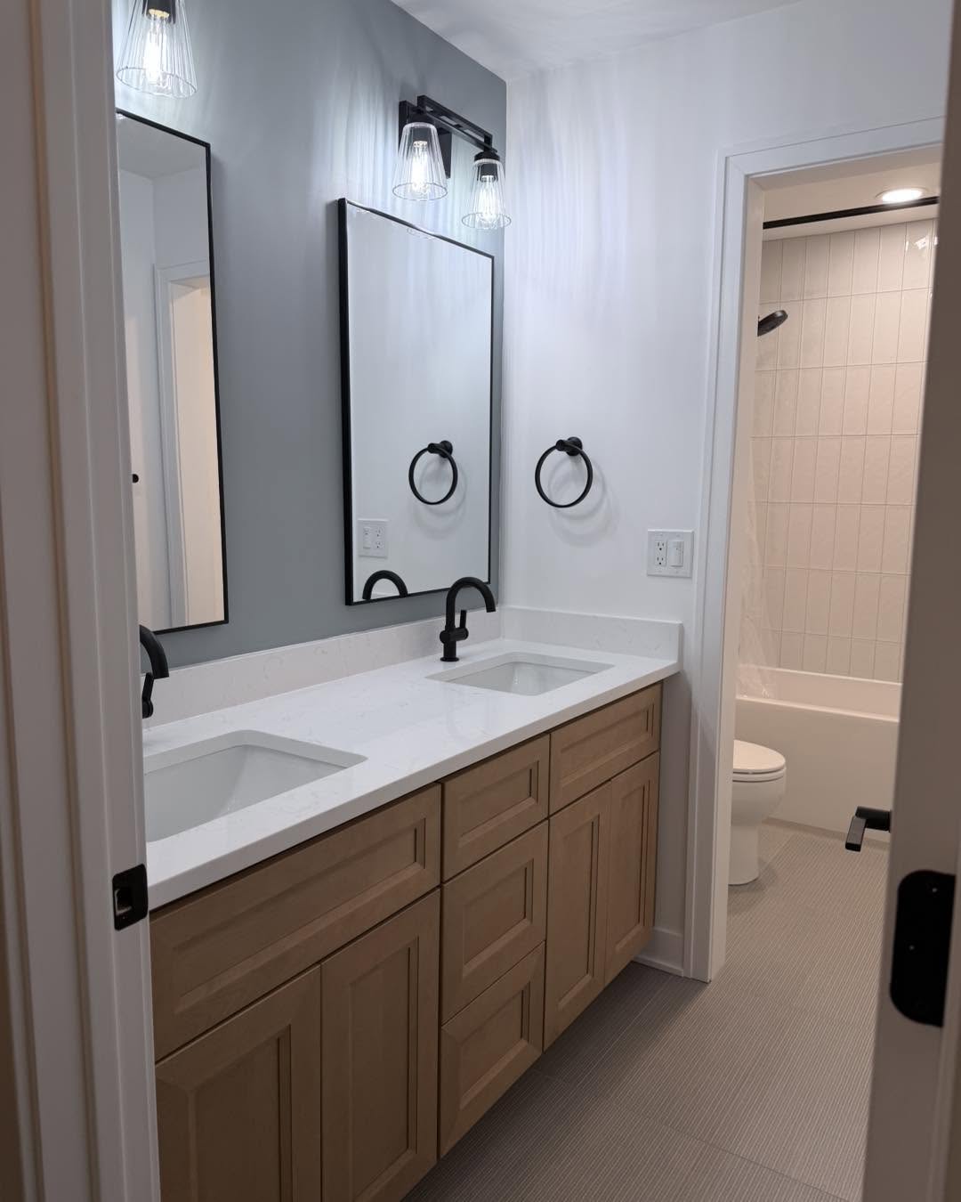 Hall bath with double wood vanity, quartz top and black fixtures by Fisher Remodeling