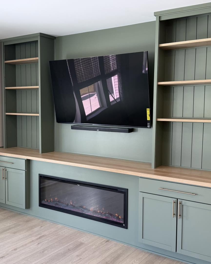 Custom sage green cabinetry and open shelving around mounted TV by Fisher Remodeling