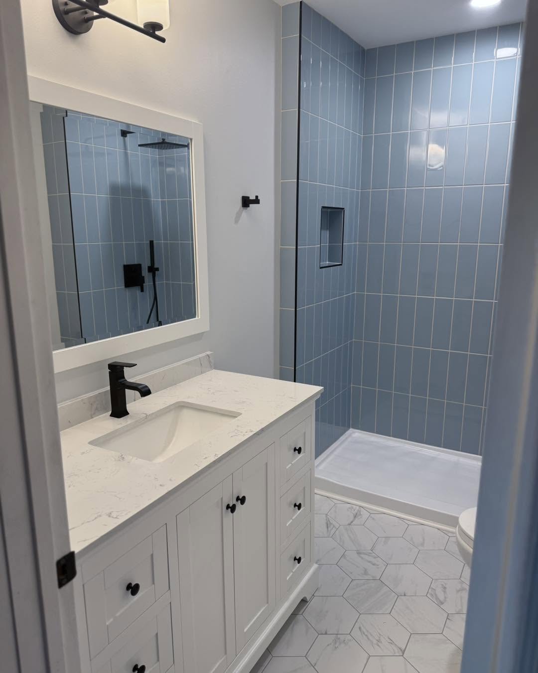 White vanity with marble countertop beside blue tiled shower by Fisher Remodeling