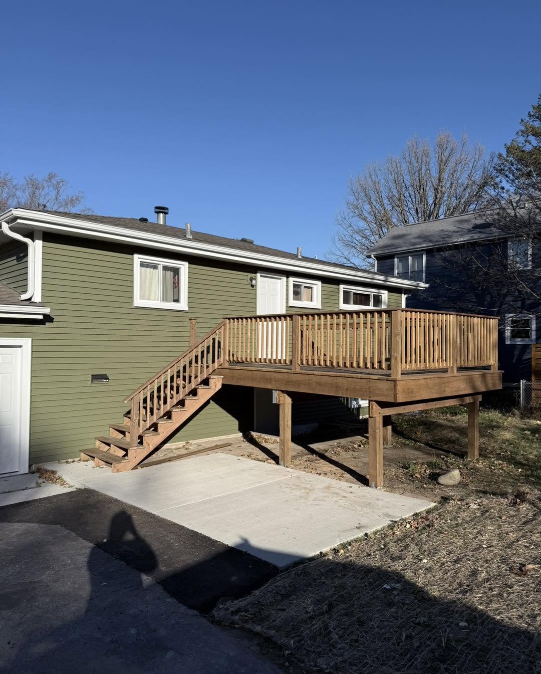 Wood deck with stairs and railings beside a green-sided home by Fisher Remodeling
