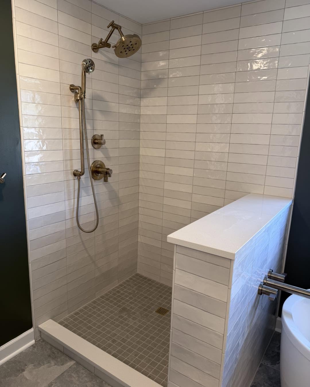 Cream tile walk-in shower with brass fixtures and pony wall by Fisher Remodeling