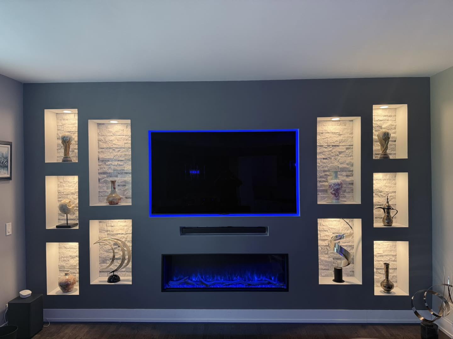 Custom media wall with LED-backlit niches and electric fireplace by Fisher Remodeling