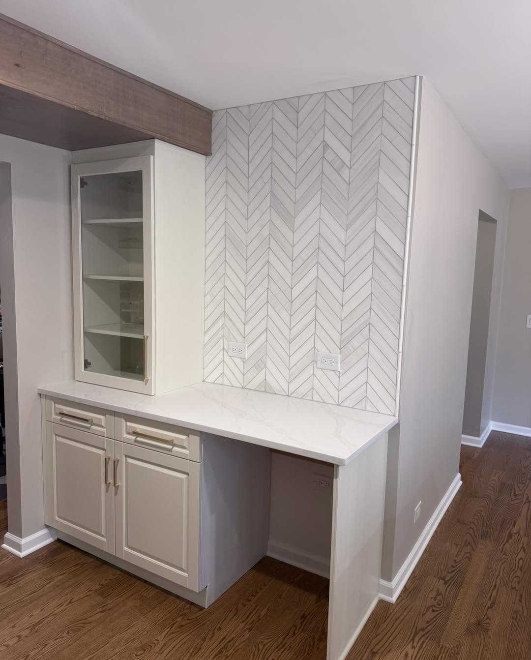 Coffee station with herringbone marble tile and cream cabinetry by Fisher Remodeling
