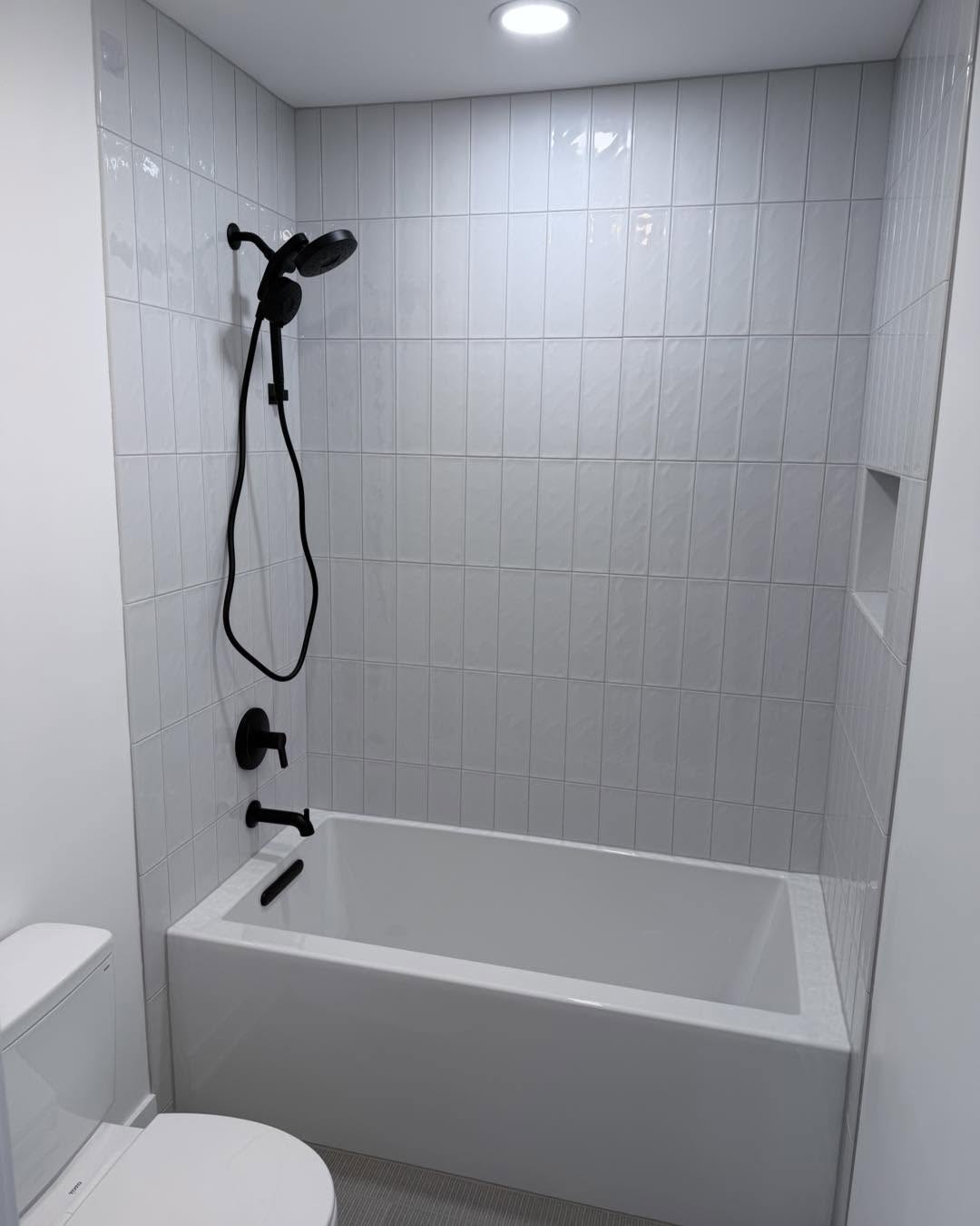 White vertical tile tub surround with matte black fixtures by Fisher Remodeling